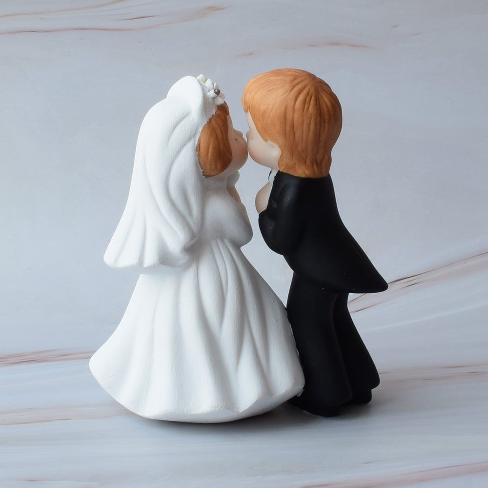 Figura para pastel de bodas con pareja de novios dándose un beso sobre mármol.