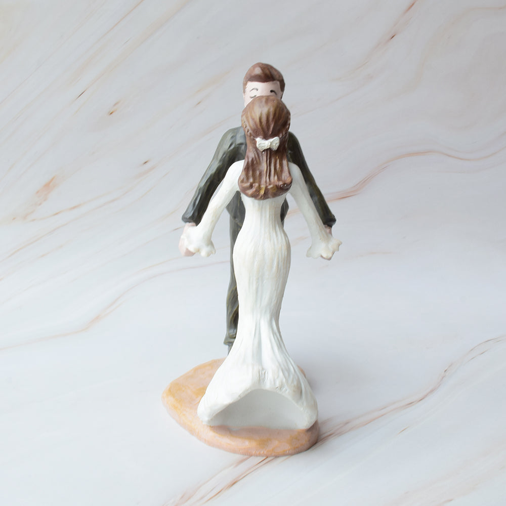 Figura para pastel de bodas en cerámica con novios dándose un dulce beso, sobre fondo de mármol.