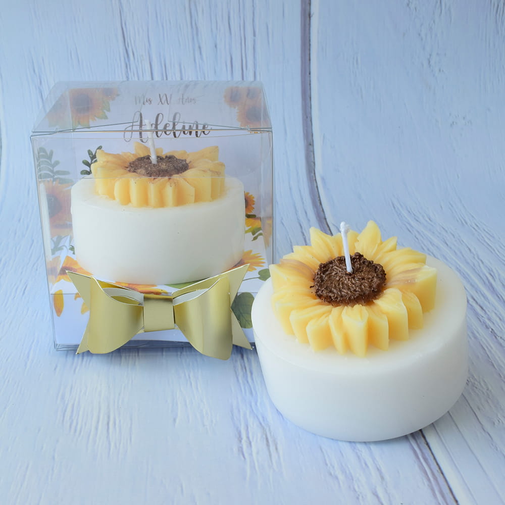 Vela blanca con diseño de girasol empacada en una caja transparente con moño dorado y personalización, ideal para recuerdo de quince años en CDMX.