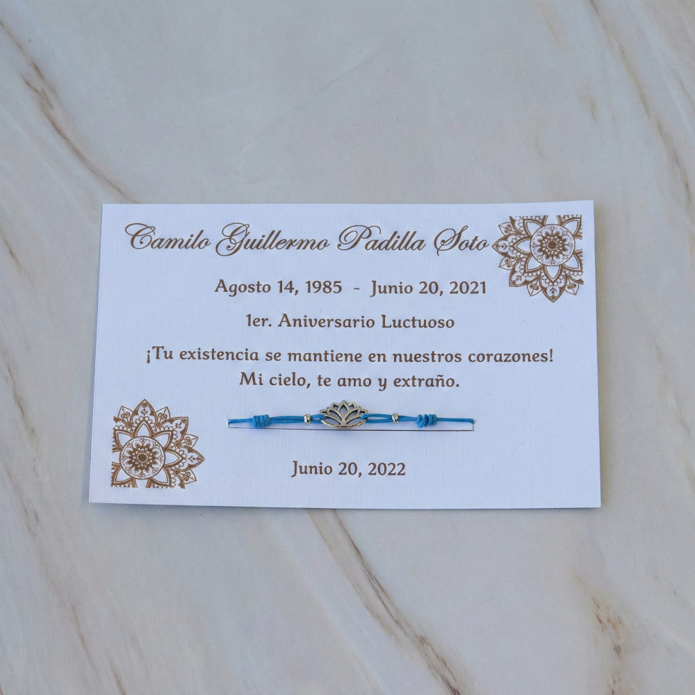 Pulsera de hilo azul con dije de flor de loto, presentada en tarjeta personalizada con diseño de mandalas, ideal como recuerdo para aniversario luctuoso.