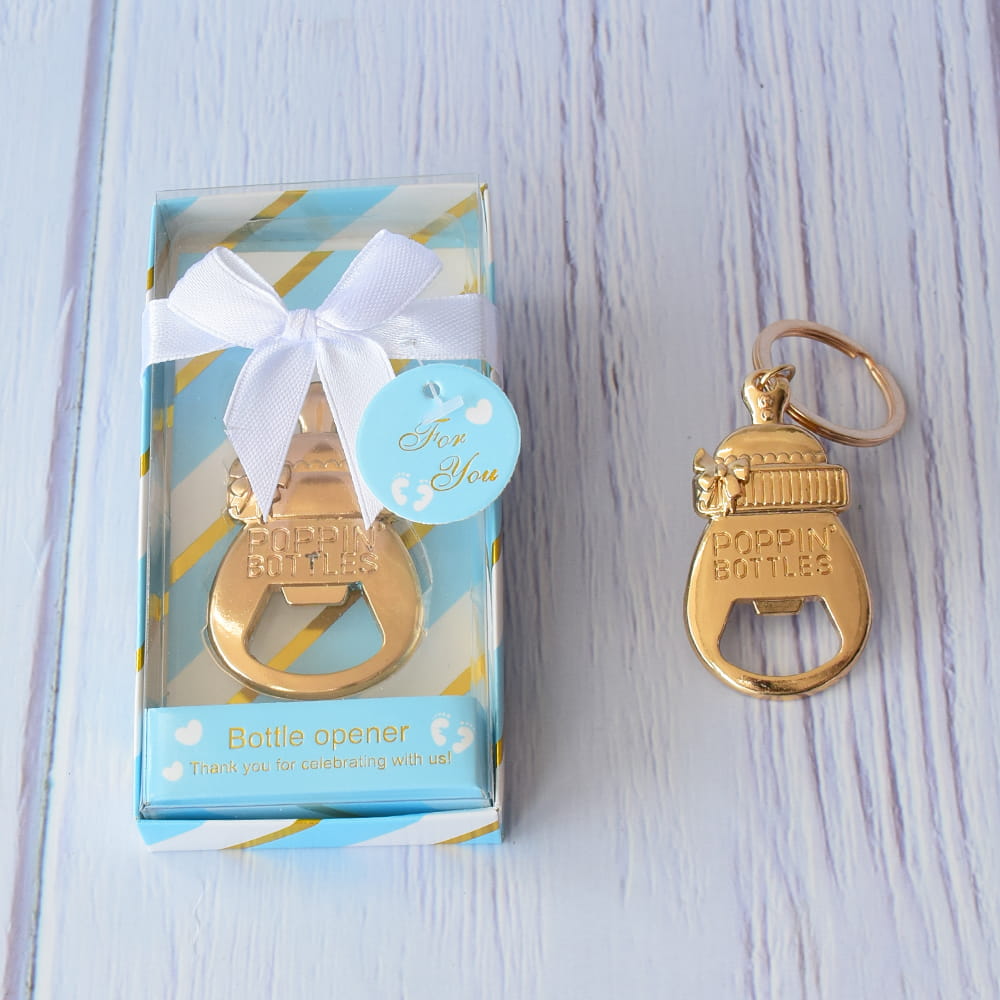 Destapador dorado en forma de biberón para recuerdo de baby shower, presentado en caja azul con moño blanco.