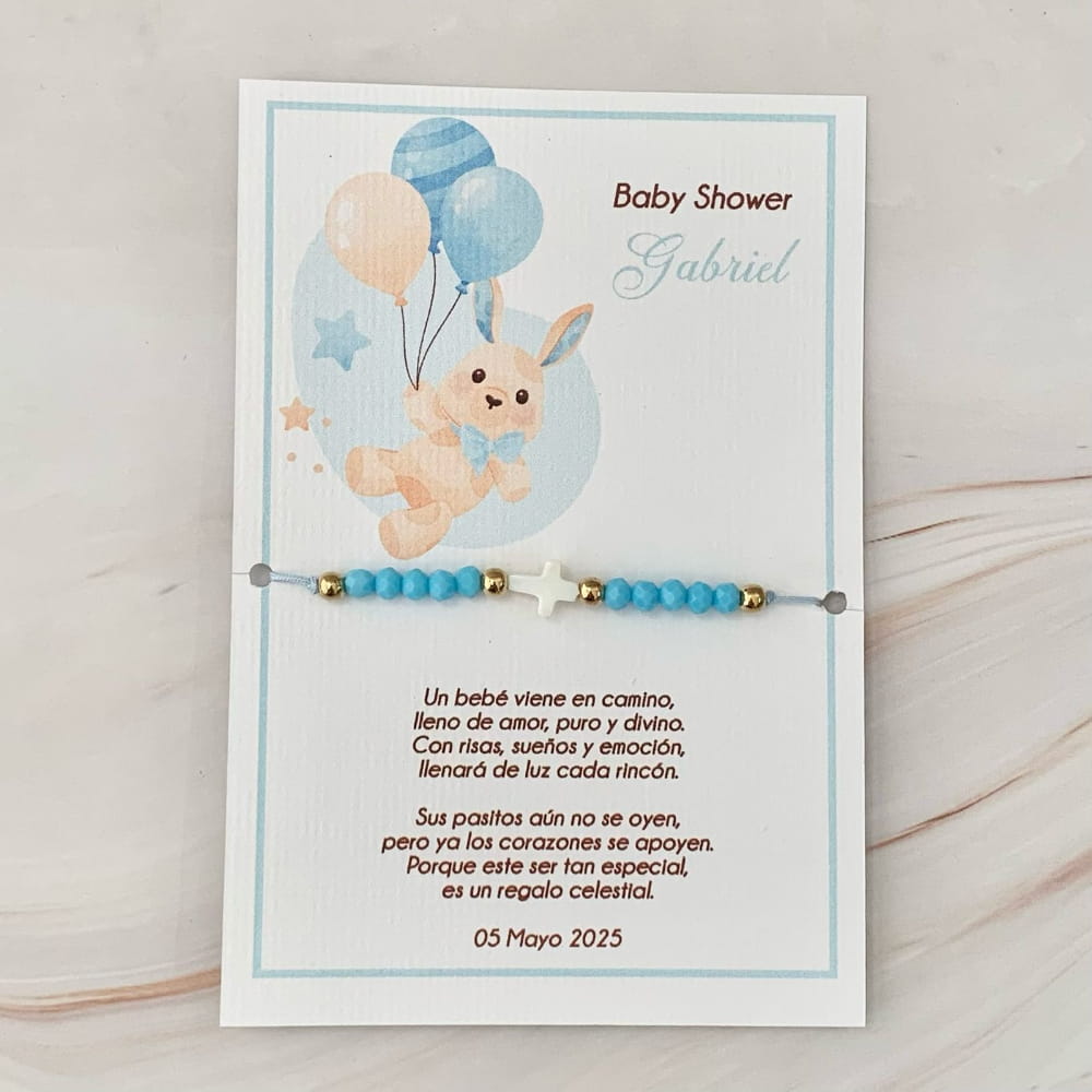 Recuerdo de Baby Shower personalizado para niño. Tarjeta decorativa con diseño infantil, poema de agradecimiento y pulsera tejida ajustable con cuentas azules y dije de cruz blanca, exhibida sobre un fondo de mármol.