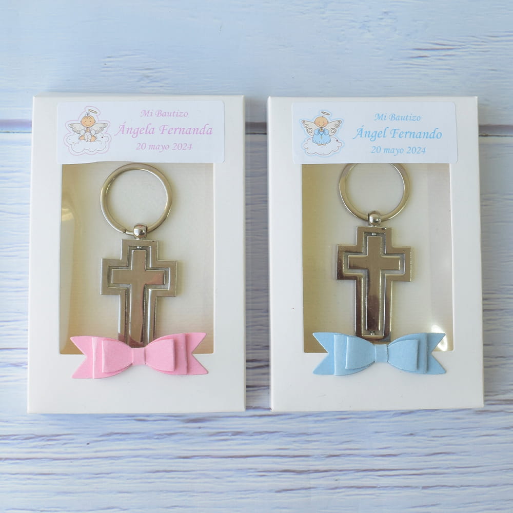 Recuerdos para bautizo de niño y niña: Llaveros de cruz metálica, empacados en cajas de regalo blancas con moños decorativos y etiquetas personalizadas.