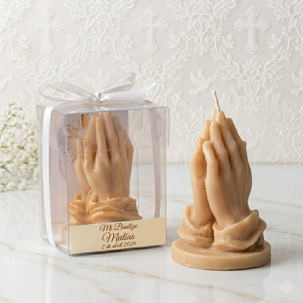 Vela artesanal en forma de manos en oración para bautizo, presentada en caja transparente con etiqueta personalizada y listón.