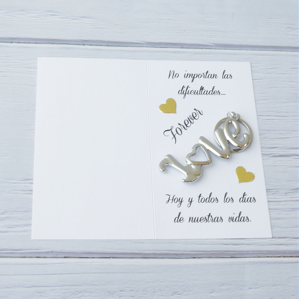 Llavero metálico con la palabra Love y tarjeta personalizada con mensaje romántico, presentado sobre fondo de madera blanca.