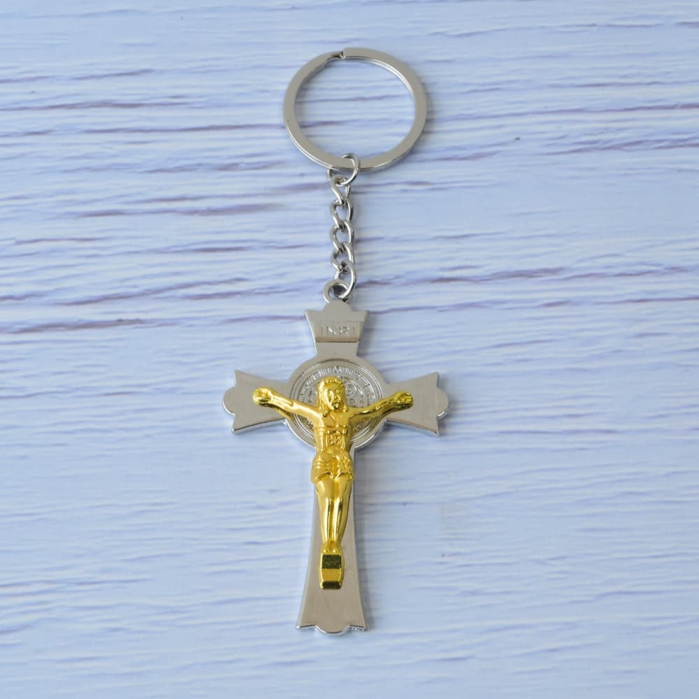 Llavero de cruz metálica plateada con figura de Cristo en acabado dorado y medalla de San Benito, recuerdo religioso y luctuoso elegante.