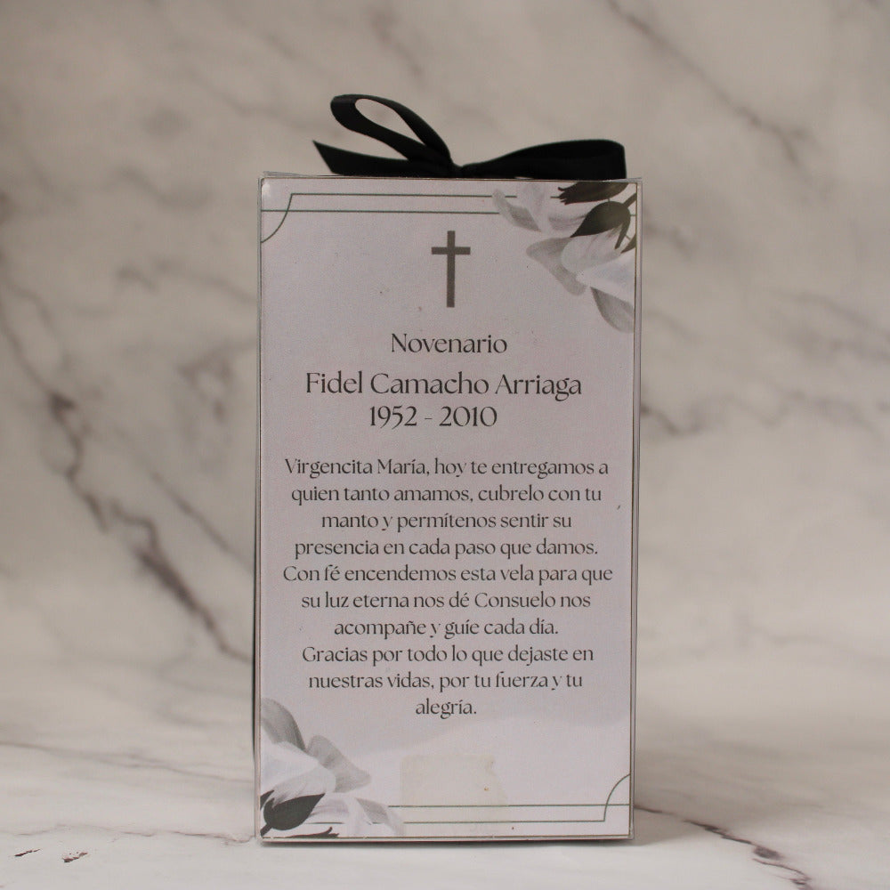 Vela artesanal en forma de Virgen con niño, presentada en caja transparente con listón negro sobre fondo de mármol.