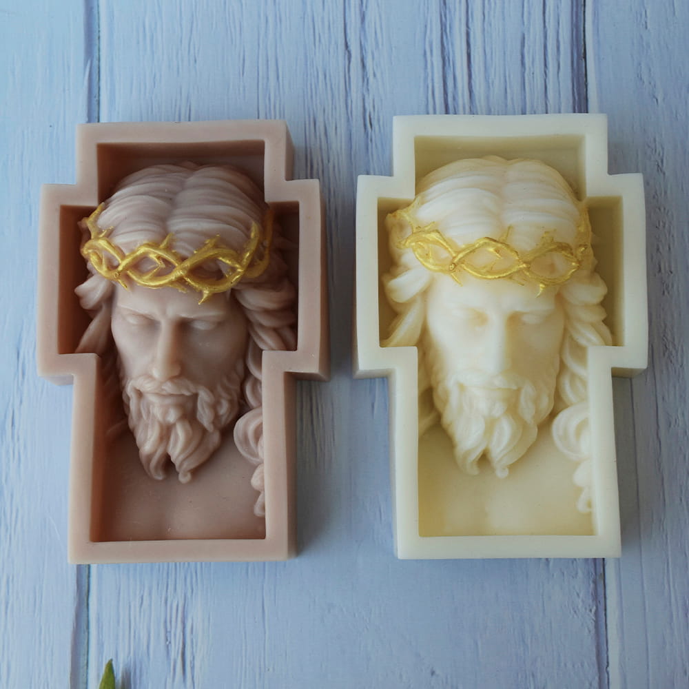 Dos velas artesanales en forma de cruz con el rostro esculpido de Cristo y corona de espinas dorada.