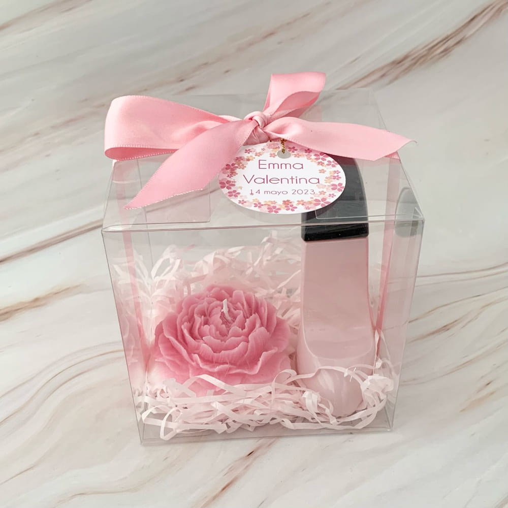Caja de regalo transparente con listón rosa. Contiene una vela en forma de flor, un perfume de zapatilla y una etiqueta personalizada