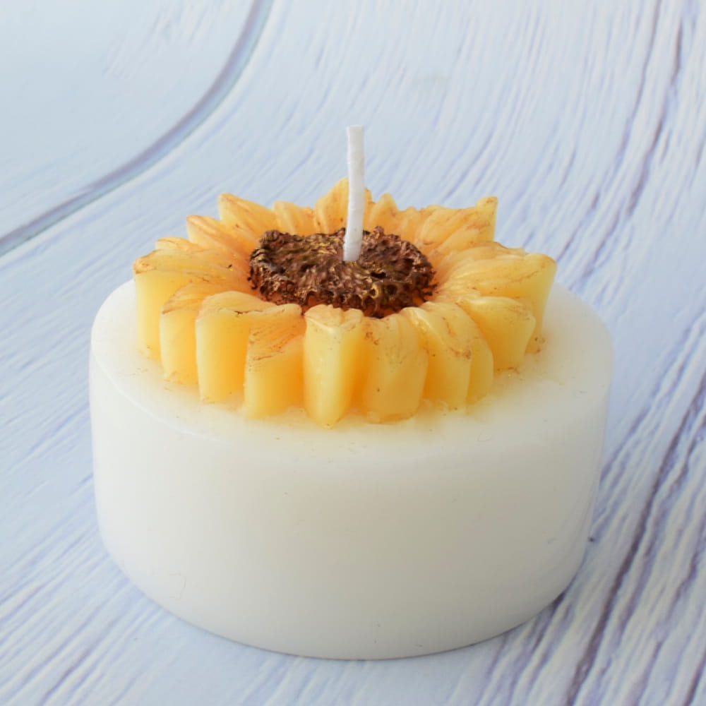 Pequeña vela artesanal blanca decorada con un girasol amarillo en relieve, ideal como recuerdo de quinceaños