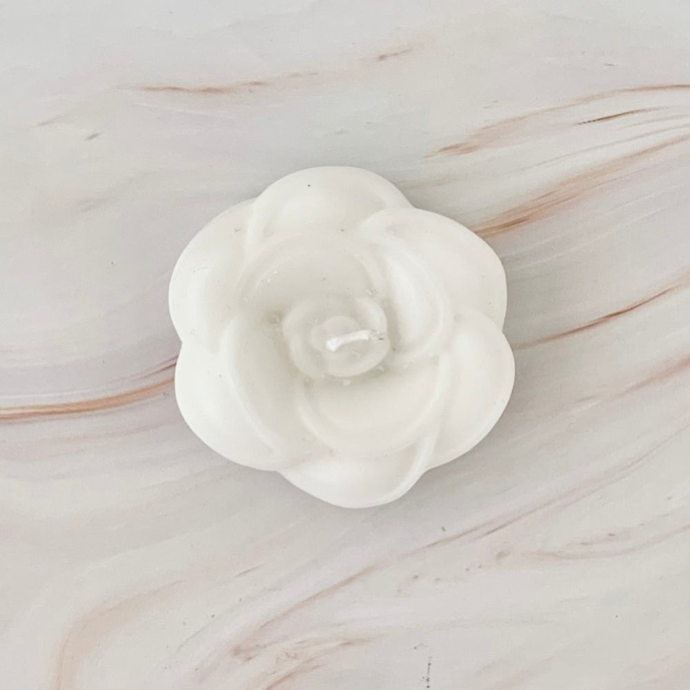 Recuerdo de velita artesanal en forma de flor blanca sobre base de mármol beige.