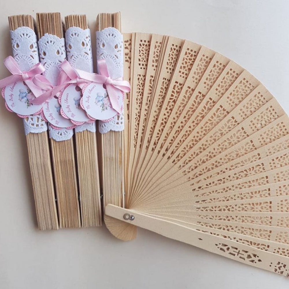 Abanicos de madera calados con envoltorio de encaje blanco, moño rosa y etiquetas personalizadas para recuerdos de baby shower.