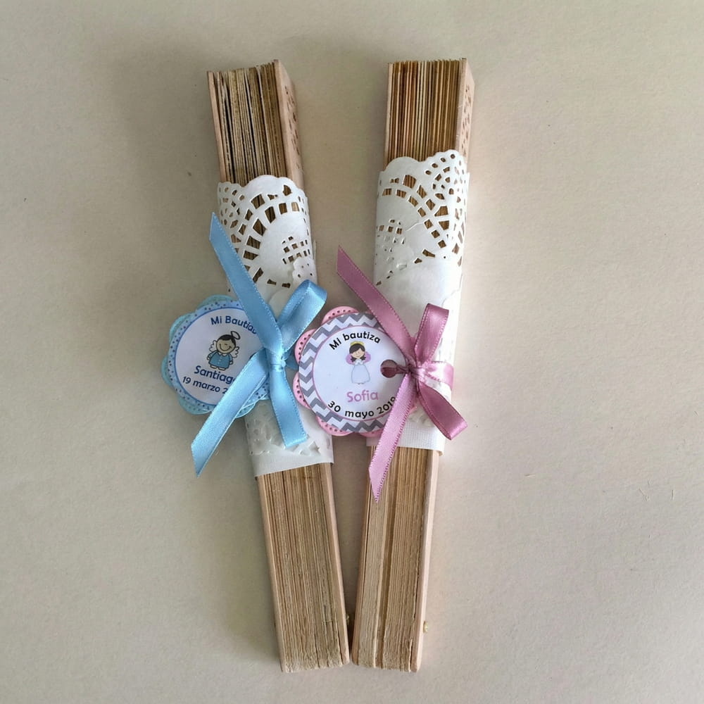Abanicos de madera presentados con blondas de papel, moños de listón y etiquetas personalizadas, ideales como recuerdos para bautizo de niño o niña.