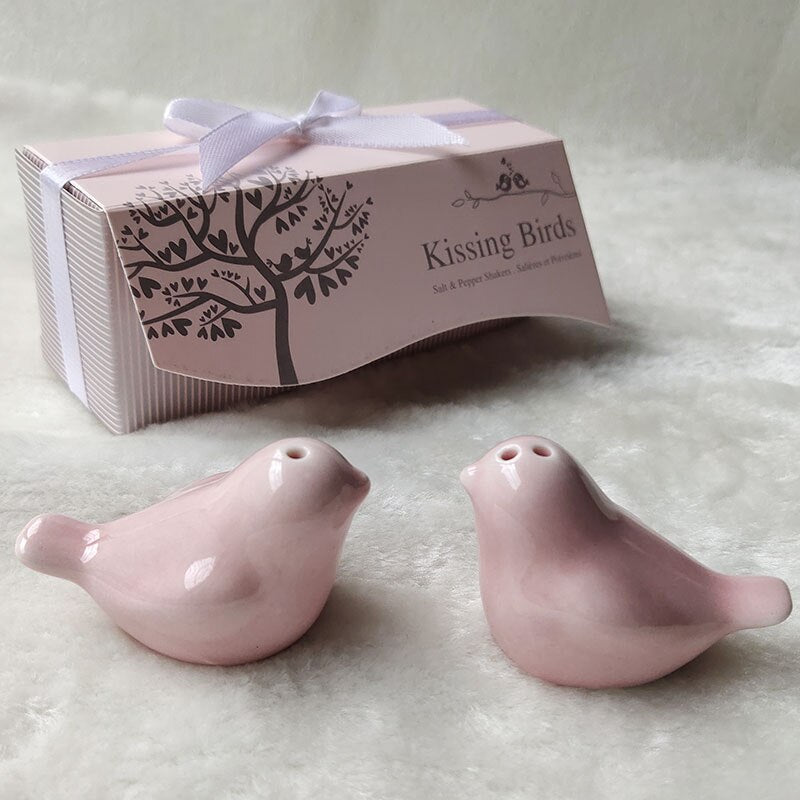 Set de salero y pimentero de cerámica en forma de pajaritos color rosa pastel, presentados dentro de una cajita decorada con árboles, ventana transparente y listón blanco.