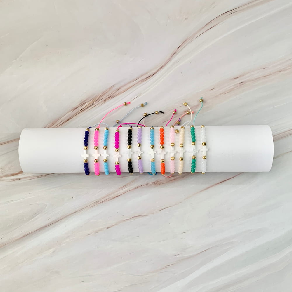 Recuerdos para eventos religiosos: Variedad de pulseras ajustables de colores con dije de cruz blanca y detalles dorados, ideales como recuerdo para bautizo, primera comunión o confirmación.