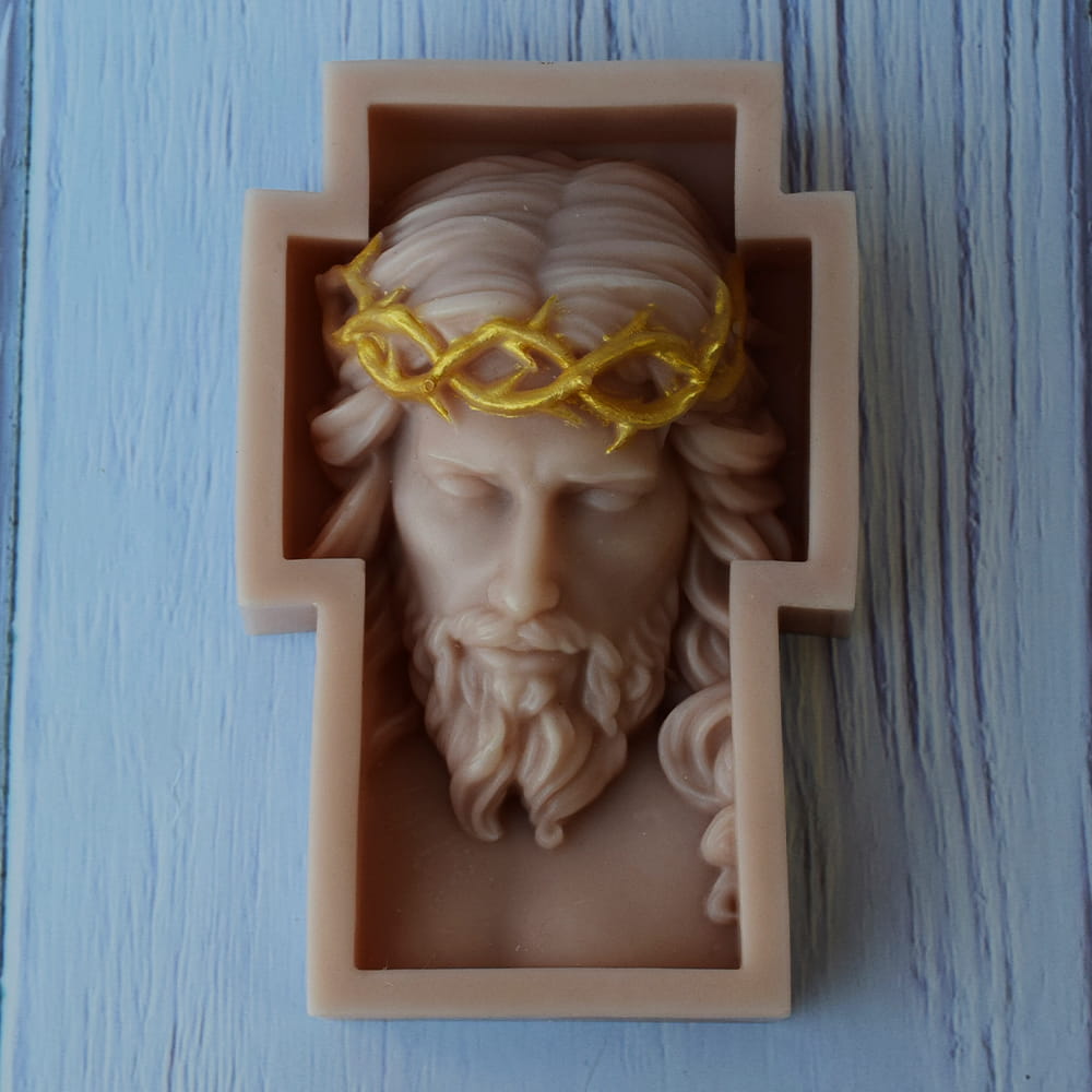 vela artesanal en forma de cruz con el rostro esculpido de Cristo y una corona de espinas dorada.