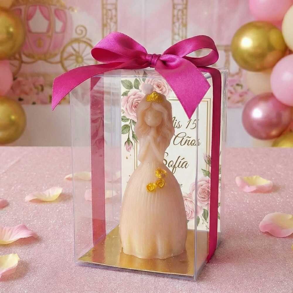 Vela artesanal en forma de quinceañera con vestido de gala y detalles dorados, recuerdo personalizado para XV años en caja de acetato con moño fucsia.