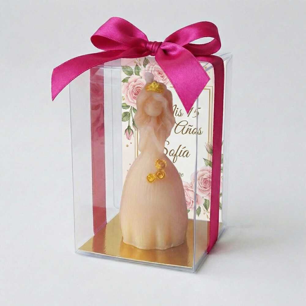 Vela artesanal en forma de quinceañera con vestido de gala y detalles dorados, recuerdo personalizado para XV años en caja de acetato con moño fucsia.