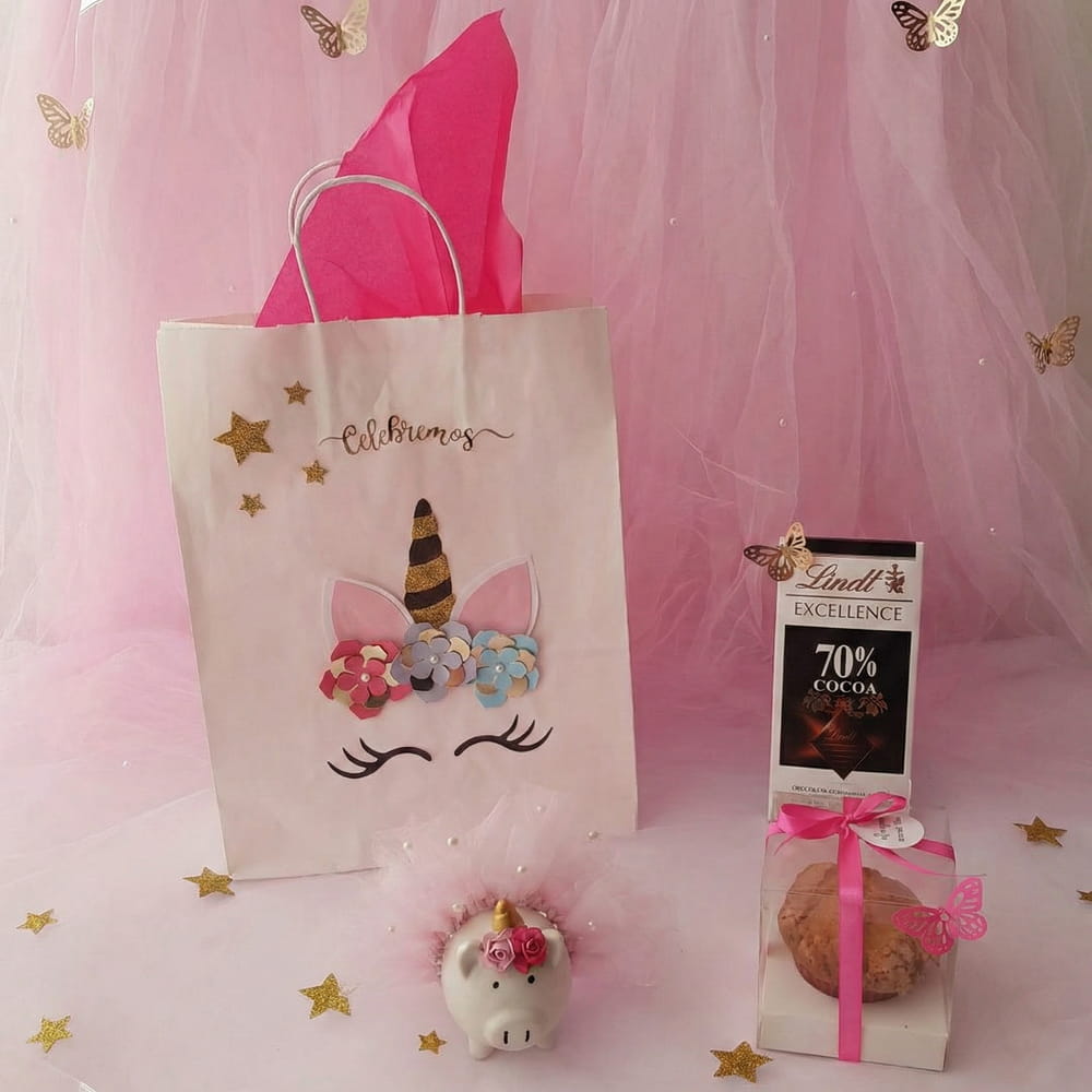 Kit de regalo con bolsa de unicornio, chocolate, muffin en caja decorada y pequeña alcancía de puerquito con tutú, ideal para cumpleaños o eventos infantiles.