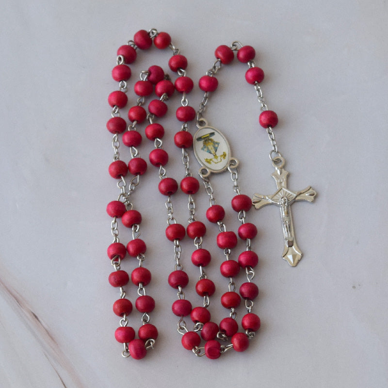 Rosario de madera de palo de rosa con cuentas rojas y crucifijo plateado, ideal como recuerdo para eventos religiosos.