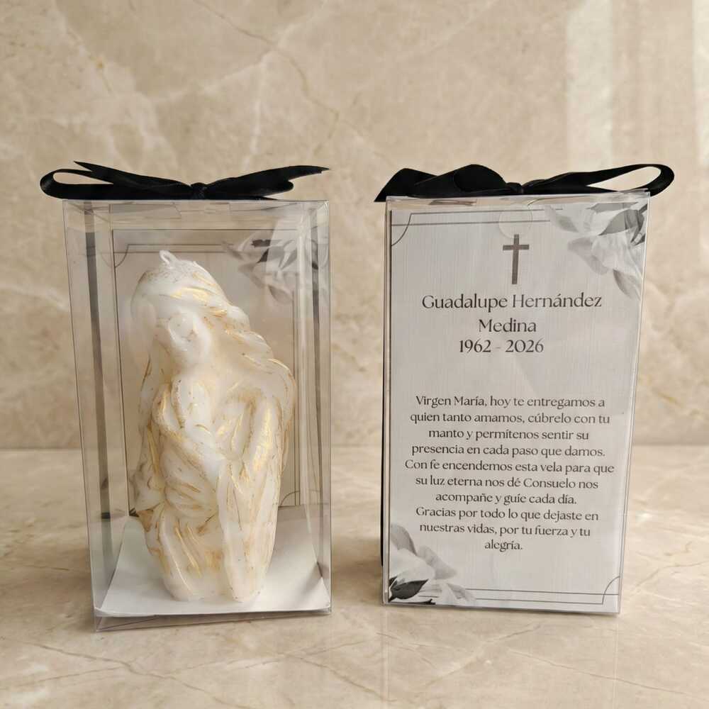 Emotivo recuerdo luctuoso con la figura de la Virgen María abrazando al niño Jesús, resaltada con sutiles toques dorados. Se muestra junto a su elegante empaque transparente con moño negro y una tarjeta que incluye una hermosa oración para honrar la memoria de un ser querido con amor y respeto.